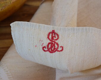 May include: A white linen fabric with a red embroidered monogram of the letter "S".