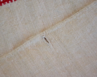 May include: Close-up of a beige linen fabric with a small hole in the center. The fabric has a woven texture and a slightly rough surface.