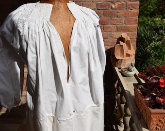May include: A white, long-sleeved garment with a deep V-neck, displayed on a mannequin. The sleeves are voluminous, and the neckline and shoulders feature delicate lace detailing. The garment has a loose fit and appears to be made of a lightweight fabric.