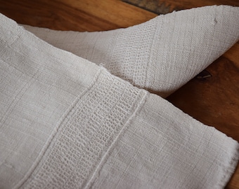 May include: A close-up of a white linen fabric with a textured weave. The fabric is folded in half, revealing the intricate pattern of the weave.