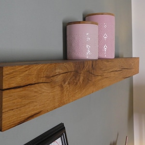 Puede incluir: Una estanter&iacute;a de madera r&uacute;stica con un acabado de madera natural, montada en una pared gris. Dos tarros de cer&aacute;mica rosa con un patr&oacute;n floral se muestran en la estanter&iacute;a.