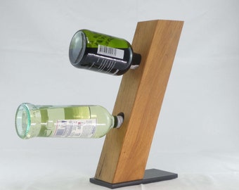 Puede incluir: Un soporte de botellas de vino de madera con una base negra. Dos botellas de vino se muestran en el soporte, una verde y una transparente.