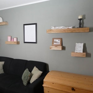 Puede incluir: Una sala de estar con una pared gris y un sof&aacute; negro. Hay varias estanter&iacute;as de madera en la pared con varios art&iacute;culos decorativos, incluyendo una figurita blanca, velas rosas, una foto enmarcada y una hoja de papel enmarcada con el texto "Et voici la monde".