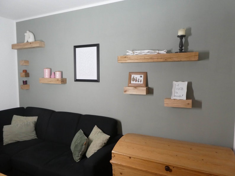 Puede incluir: Una sala de estar con una pared gris y un sof&aacute; negro. Hay varias estanter&iacute;as de madera en la pared con varios art&iacute;culos decorativos, incluyendo una figurita blanca, velas rosas, una foto enmarcada y una hoja de papel enmarcada con el texto "Et voici la monde".