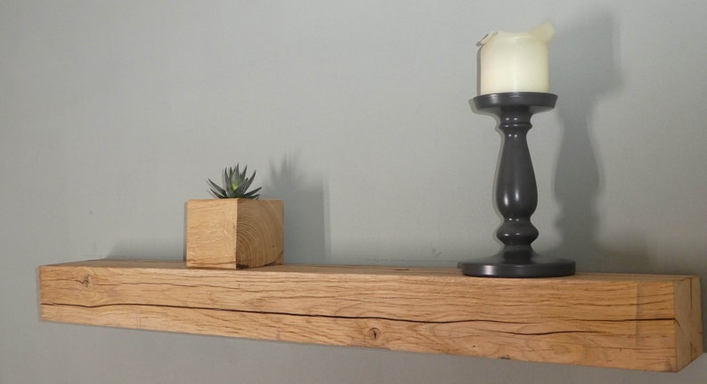 Puede incluir: Una estanter&iacute;a de madera r&uacute;stica con un acabado de madera natural, que presenta una peque&ntilde;a planta suculenta en una maceta de madera y un candelero negro con una vela blanca en la parte superior.
