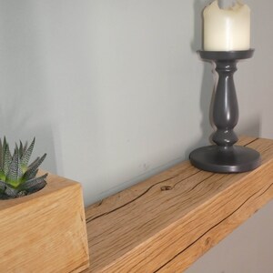Puede incluir: Una estanter&iacute;a de madera con un acabado de madera natural y una peque&ntilde;a planta suculenta en una maceta de madera. Un candelero negro con una vela blanca est&aacute; en la estanter&iacute;a.