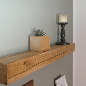 Puede incluir: Una estanter&iacute;a de madera r&uacute;stica con un acabado de madera natural. La estanter&iacute;a est&aacute; montada en una pared verde claro y presenta una peque&ntilde;a planta suculenta en una maceta de madera y un candelero negro con una vela blanca.