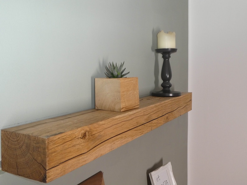 Puede incluir: Una estanter&iacute;a de madera r&uacute;stica con un acabado de madera natural. La estanter&iacute;a est&aacute; montada en una pared verde claro y presenta una peque&ntilde;a planta suculenta en una maceta de madera y un candelero negro con una vela blanca.
