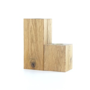 May include: A wooden candle holder with two rectangular blocks, one with a small round cutout for a candle. The wood is a light brown colour with a natural grain pattern.