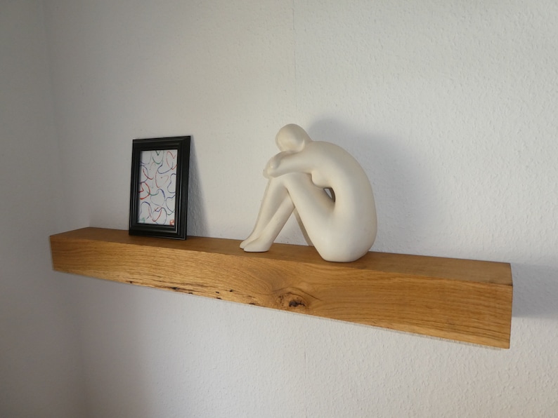 Puede incluir: Una estanter&iacute;a de madera con una escultura de cer&aacute;mica blanca de una persona sentada sobre ella. Un cuadro enmarcado con un dise&ntilde;o abstracto de colores est&aacute; en el lado izquierdo de la estanter&iacute;a.