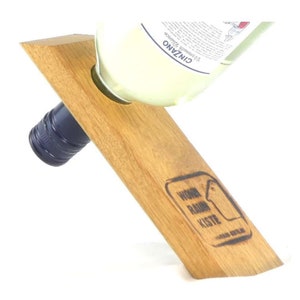 May include: Wooden wine bottle holder with a cutout for the bottle neck. The holder is angled and has the text "WOHN RAUM KISTE" burned into the wood.