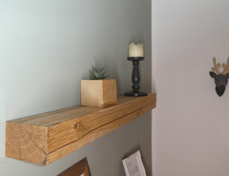 Puede incluir: Una estanter&iacute;a de madera r&uacute;stica con una peque&ntilde;a planta suculenta en maceta, un candelero negro con una vela blanca y una cabeza de reno de madera montada en la pared.