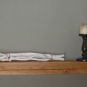 Puede incluir: Una estanter&iacute;a de madera r&uacute;stica con una decoraci&oacute;n de ramas blancas y un candelero negro con una vela blanca en la parte superior.