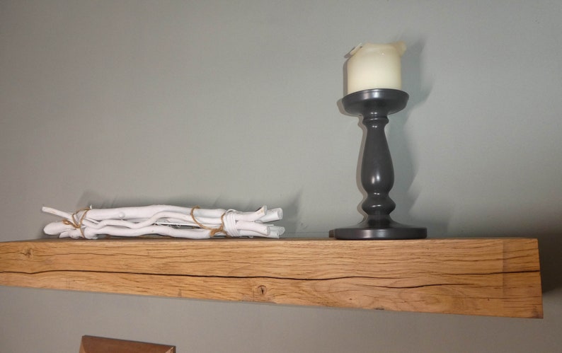 Puede incluir: Una estanter&iacute;a de madera r&uacute;stica con un candelero blanco y un manojo de madera flotante blanca en la parte superior. La estanter&iacute;a est&aacute; hecha de madera natural con un nudo y un patr&oacute;n de veta.
