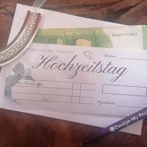 May include: A white wedding card with the German text "Hochzeitstag" and a decorative silver bookmark with clear rhinestones. A purple pen with "Design My Post" is also visible.