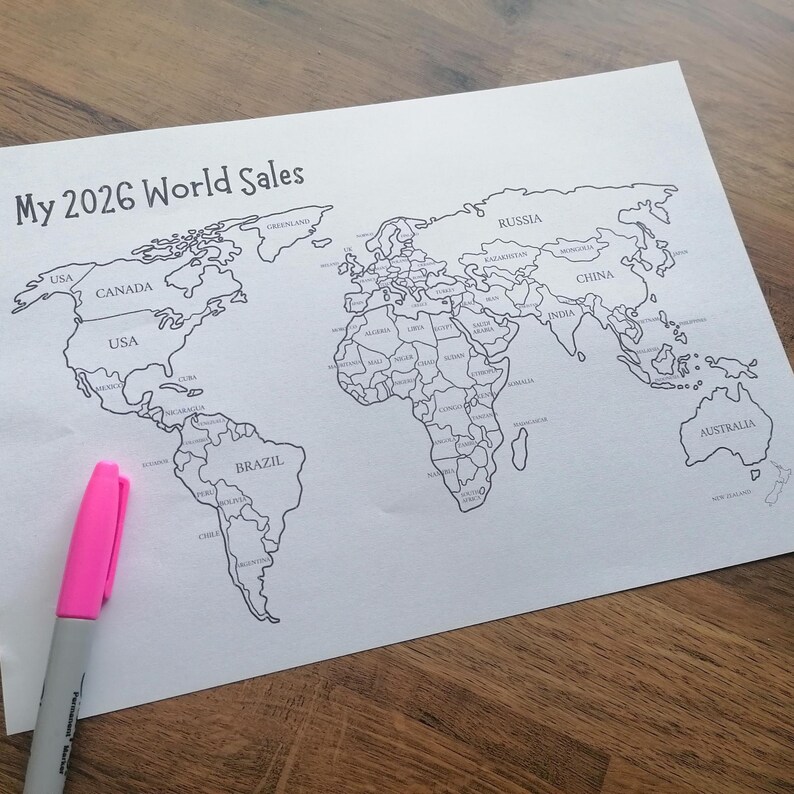 May include: A white sheet of paper featuring a black and white outline map of the world with the text My 2026 World Sales printed at the top left. A bright pink marker is positioned on the lower left side of the paper, pointing toward the map.