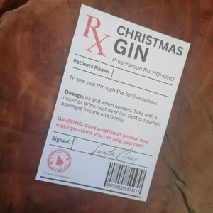 May include: A white prescription label with red text that reads "Christmas Gin" and "Prescription No: HOHOHO". The label also includes a dosage and warning about the consumption of alcohol. The label is signed "Santa Claus".