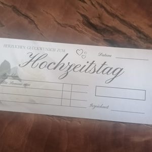 May include: A white card with the German text "HERZLICHEN GL&Uuml;CKWUNSCH ZUM HOCHZEITSTAG" in elegant script. The card includes spaces for a date, amount, and signatures, with heart illustrations.