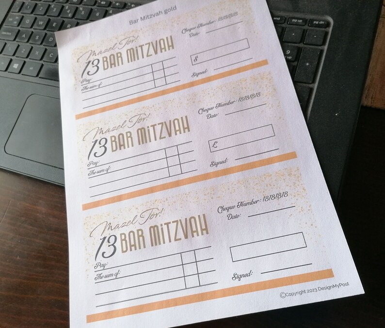 May include: A white sheet of paper featuring three printed templates for Bar Mitzvah gift cheques. Each template includes the text Mazel Tov! 13 Bar Mitzvah, with fields for cheque number, date, amount, payee, and signature, accented with gold glitter.