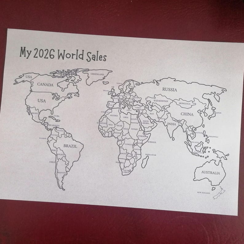 May include: A white paper sheet featuring a black line-art world map with the text My 2026 World Sales printed at the top. The map includes labeled countries such as USA, Canada, Brazil, Russia, China, and Australia, with clear borders.