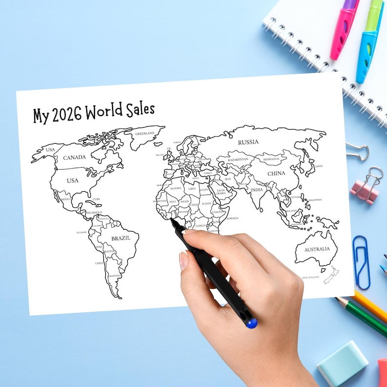 May include: A white sheet of paper featuring a black and white outline map of the world with the text My 2026 World Sales printed at the top. The map includes labeled continents and countries, with a black pen positioned over the African continent.