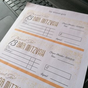 May include: A white paper sheet featuring three printed templates for Bar Mitzvah gift cheques. Each template includes the text Mazel Tov, 13 Bar Mitzvah, Pay, The sum of, Cheque Number: 18181818, Date, and Signed, with gold-colored accents and borders.