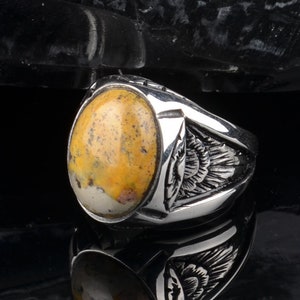 Peut inclure: Une bague en argent avec une pierre ovale jaune et blanche sertie dans un sertissage &agrave; b&eacute;li&egrave;re. La bague a un design d&eacute;taill&eacute; sur la bande.