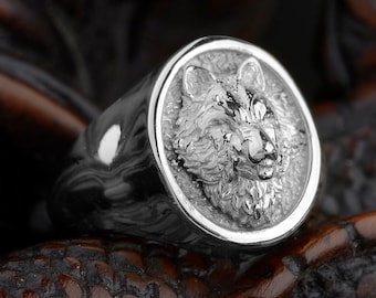 May include: A silver ring with a detailed wolf head design. The ring is on a dark brown wooden surface.