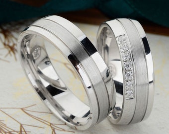 May include: Two silver wedding bands, one with a row of small diamonds, on a white background.