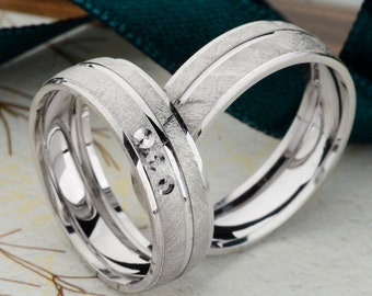 May include: Two silver wedding bands with a brushed finish. One band has three small diamonds set in a row.