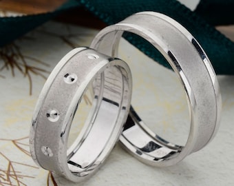 May include: Two silver wedding bands. One band has a textured finish and the other has a row of small circles.