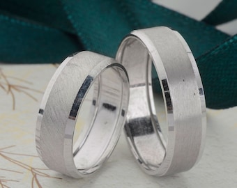 May include: Two silver wedding bands with a brushed finish. The bands are side by side on a white background.