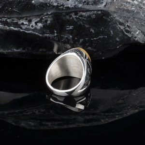 Peut inclure: Une bague en argent avec un motif dor&eacute; sur le dessus. La bague est sur une surface noire.