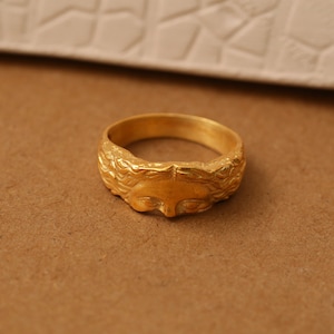 May include: A gold ring with a detailed face design. The face is surrounded by a textured, braided design.