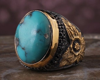 May include: A silver ring with a large turquoise stone set in a gold bezel. The ring is decorated with a floral design and black stones.