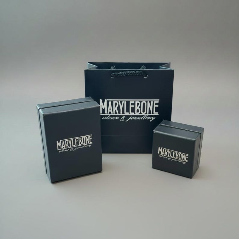 May include: A dark navy blue shopping bag and two matching jewelry boxes. The bag and boxes have the white text "MARYLEBONE silver & jewellery". The boxes are rectangular with hinged lids.