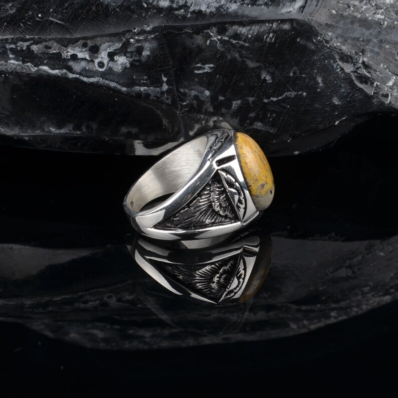 Peut inclure: Une bague en argent avec une pierre jaune et brune sertie dans un design d&eacute;taill&eacute;. La bague est sur une surface noire.