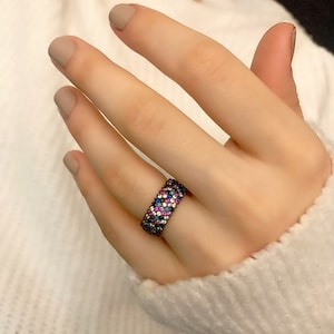 May include: A silver ring with a colorful band of small stones. The stones are arranged in a pattern of pink, blue, and white.