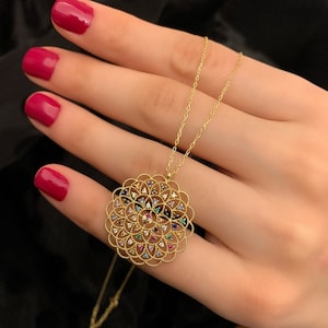 May include: A gold necklace with a round pendant featuring a delicate filigree design and colorful gemstones.
