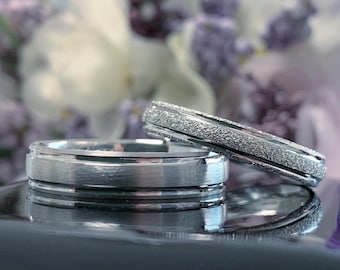 May include: Two silver wedding bands. One band has a smooth finish, while the other has a textured, brushed finish.