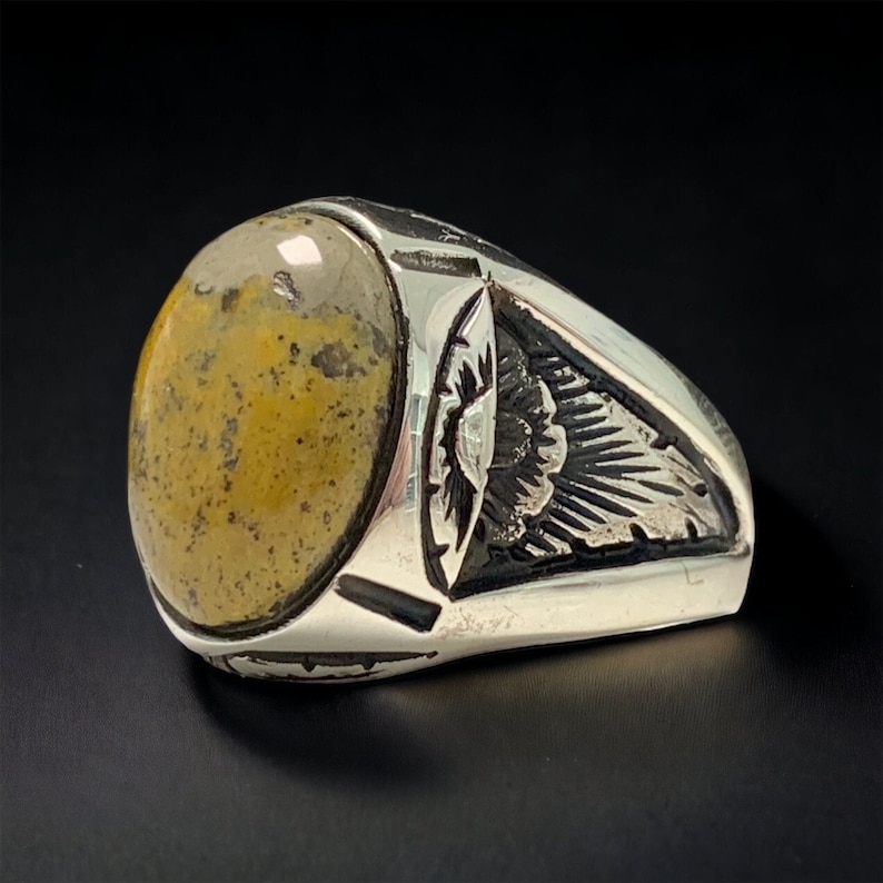 Peut inclure: Une bague en argent avec une grande pierre pr&eacute;cieuse ovale de couleur jaune et brune sertie au centre. La bande de la bague est d&eacute;cor&eacute;e d'un motif floral.