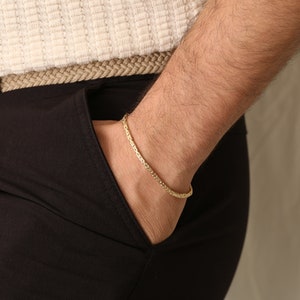 May include: A gold-colored bracelet with a textured, chain-like design. The bracelet is worn on a wrist, with the hand in a pocket. The bracelet is approximately 7 inches (17.78 cm) in length.
