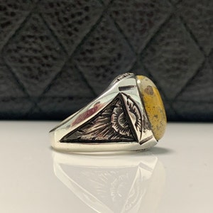 Peut inclure: Une bague en argent avec une pierre jaune et blanche sertie dans un motif d&eacute;taill&eacute;. La bague est sur un fond noir.