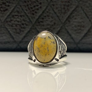 Peut inclure: Une bague en argent avec une pierre pr&eacute;cieuse en agate jaune et blanche de forme ovale. La bague a un design d&eacute;taill&eacute; sur la bande.