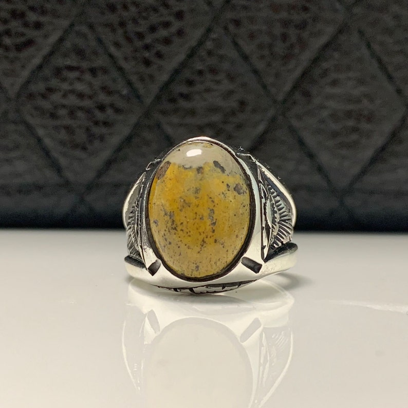 Peut inclure: Une bague en argent avec une pierre pr&eacute;cieuse en agate jaune et blanche de forme ovale. La bague a un design d&eacute;taill&eacute; sur la bande.