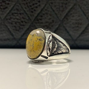 Peut inclure: Une bague en argent avec une pierre ovale jaune et brune. La bague a un design d&eacute;taill&eacute; sur la bande.