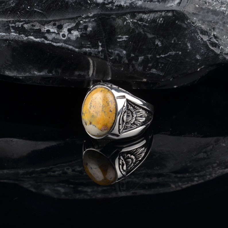 Peut inclure: Une bague en argent avec une pierre ovale jaune et blanche sertie dans un sertissage &agrave; b&eacute;li&egrave;re. La bague a un design d&eacute;taill&eacute; sur la bande.