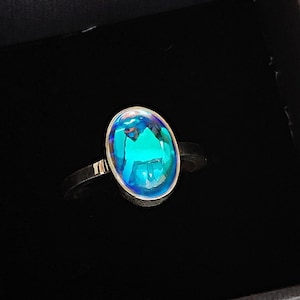 May include: A silver ring with a blue oval-shaped gemstone. The ring is in a black velvet box.