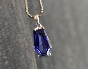May include: A silver chain necklace with a dark blue gemstone pendant. The pendant is faceted and has a geometric shape.