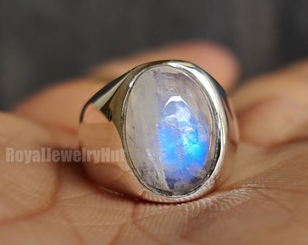 Puede incluir: Un anillo de plata con una gran piedra de luna ovalada. La piedra de luna tiene un brillo iridiscente azul.